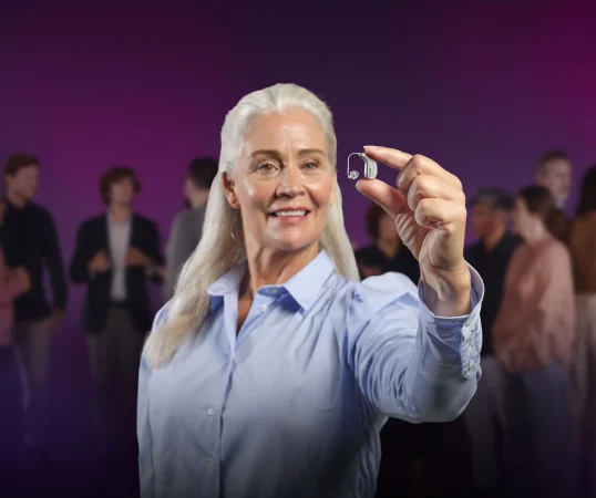 Kvinde holder et Oticon Intent høreapparat i mellem fingrene